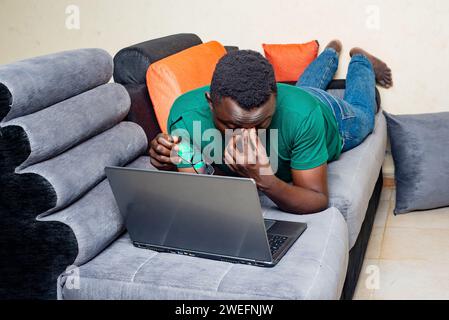 Junger Mann müde und liegend auf einem Sofa zu Hause mit einem Laptop. Stockfoto