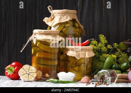 Konservierte Gurken in geschlossenen Gläsern, frische Gurken, Gemüse und Gewürze für Marinade auf hölzernem Hintergrund. Stockfoto