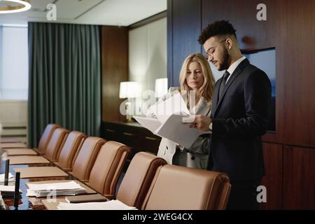 Eine kaukasische Anwältin und ihr männlicher Kollege aus dem Mittleren Osten sehen sich die Papiere in der Vorstandssitzung an Stockfoto