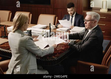 Leitender Anwalt, der Papier an seine Kollegin weitergibt, ein Mann aus dem Nahen Osten, der Papiere über Hintergrund liest Stockfoto