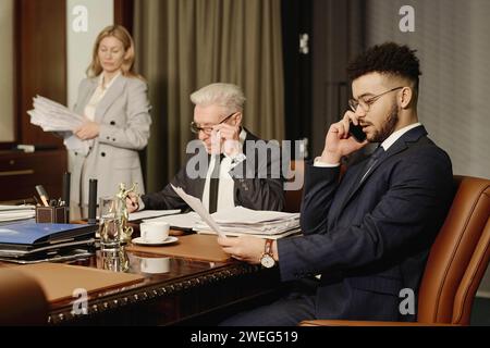 Junger Anwalt aus dem Nahen Osten, der geschäftlich telefoniert, seine Kollegen machen Papierkram in der Nähe Stockfoto