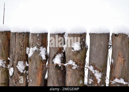 Vintage-Holzzaun, Holzpfosten, vertikale Baumstämme bedeckt mit weißem flauschigem Schnee. Winterlandschaft, kaltes Wetter, strukturierte Details. Stockfoto