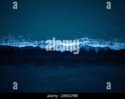 Majestic view of dark blue ocean waves splashing black sand beach, aerial top down shot. Dynamic background and natural beauty concepts. Stockfoto