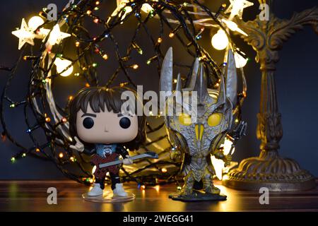 Funko Pop Actionfiguren von Eddie aus Stranger Things und Sauron aus dem Herr der Ringe. Orangefarbene Beleuchtung, schwarzer Hintergrund, bunte Girlande. Stockfoto