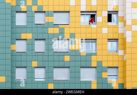 Hauptfassade eines bunten karierten Gebäudes mit einer Frau in Rot, die ein Fenster putzt, in Oviedo, Asturien, Spanien Stockfoto