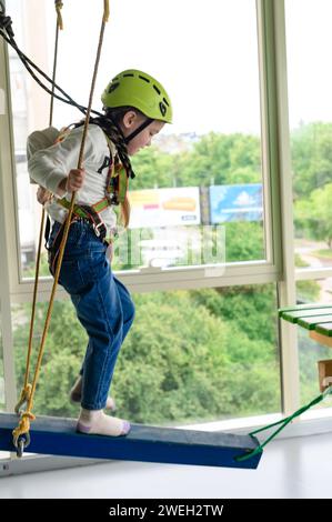 Kinderseilbahn im Spielzimmer passiert das kleine Mädchen die Seilbahn, die aktive und körperliche Entwicklung des Kindes. Stockfoto