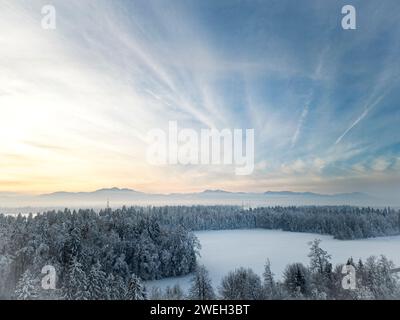 Foto mit einer Drohne von einer wunderschönen, schneebedeckten Winterlandschaft - Wald und eine Lichtung mit Bergen in der Ferne unter dem wunderschönen blauen Himmel mit ge Stockfoto