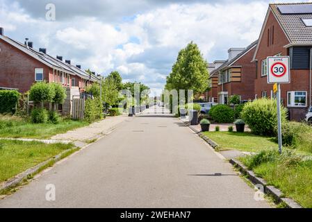 An einem bewölkten Sommertag in einem vorstädtischen Wohnviertel, gesäumt von Einfamilienhäusern aus Ziegelsteinen. Die Mülltonnen sind entlang der Straße. Stockfoto