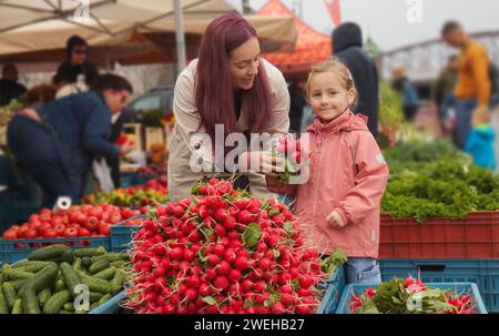 Ein kleines Mädchen mit frischen Radishies und ihre junge Mutter kaufte Gemüse auf dem Bauernmarkt in Prag. Stockfoto