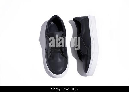 Schwarze Sneakers auf weißem Hintergrund, Draufsicht mit harten Schatten. Damenschuhe. Stockfoto