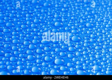 Viele kleine blaue Tropfen Wasser auf einer blauen Oberfläche Stockfoto