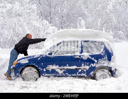 Ein Mann befreit sein blaues Kompaktauto aus einem halben Meter Neuschnee, München ca. 2006, Bayern, Deutschland, Europa Stockfoto