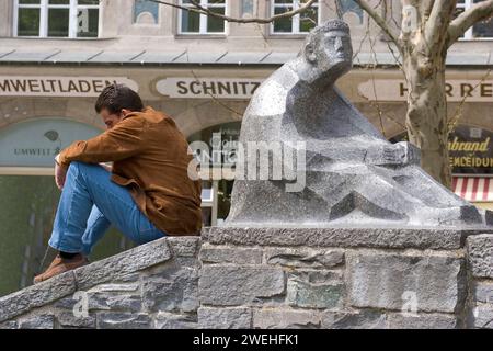 Ein Mann, der genau in derselben Position sitzt wie eine Steinfigur neben ihm, Rindermarktbrunnen, München, Bayern, Deutschland, Europa Stockfoto