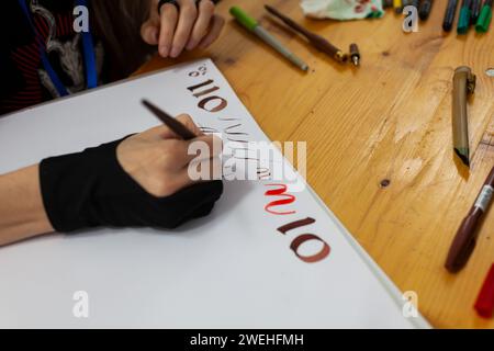 Eine erfahrene Kalligrafin übt das Schreiben und Zeichnen von Schriften im Stil der Renaissance in einem Skizzenbuch. Auf dem Holztisch gibt es Markierungen und Farben Stockfoto