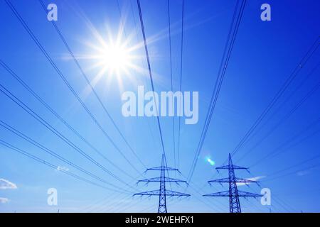 Zwei Hochspannungsmasten mit Hochspannungsleitungen, die von blauem Himmel und Sonne hinterleuchtet werden Stockfoto