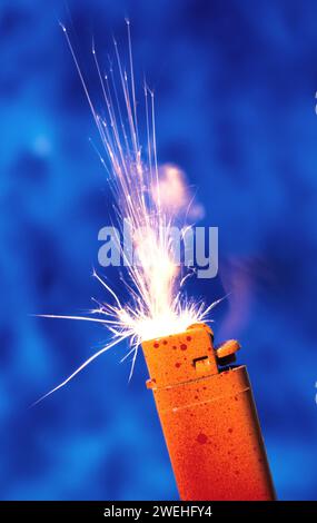 Ein orange-rotes Feuerzeug sprüht Funken vor blauem Hintergrund Stockfoto