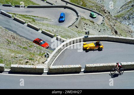 Ein rot-grün-blaues Auto, ein gelber Caterham Seven und ein Fahrradfahrer in Haarnadelkurven auf dem Stilfserjoch, Südtirol, Italien, Europa Stockfoto