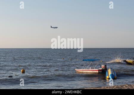 Ein Flugzeug, das über das karibische Meer fliegt, von einem Resort-Strand aus in der goldenen Stunde des Sonnenuntergangs gesehen Stockfoto