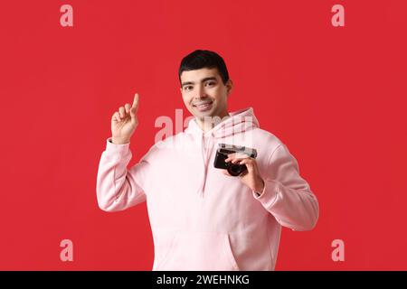 Junger männlicher Fotograf mit Kamera, der auf etwas auf rotem Hintergrund zeigt Stockfoto
