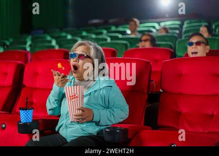 Ältere asiatische Frau, die beim Anschauen eines Horrorfilms im Kino echtes Erstaunen ausdrückt Stockfoto