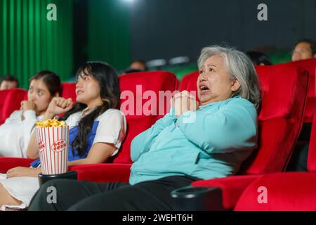 Ältere asiatische Frau, die beim Anschauen eines Horrorfilms im Kino echtes Erstaunen ausdrückt Stockfoto