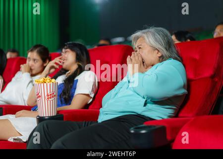 Ältere asiatische Frau, die beim Anschauen eines Horrorfilms im Kino echtes Erstaunen ausdrückt Stockfoto