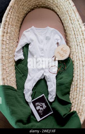 Draufsicht auf Babykleidung und Ultraschallfoto im moses Korb. Wir erwarten ein neues Leben. Vorbereitung auf das Neugeborene-Konzept. Stockfoto