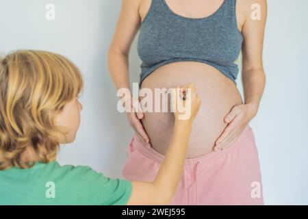 Ein entzückender Moment, in dem ein Sohn der Schwangerschaft seiner Mutter einen Hauch Freude verleiht, indem er spielerisch ein lustiges Gesicht auf ihre Babyhöhle zieht und so wertvolle Erinnerungen schafft Stockfoto