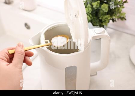 Reinigen des elektrischen Wasserkochers. Frau, die Backpulver in das Gerät am Tisch einfüllte, über der Ansicht Stockfoto