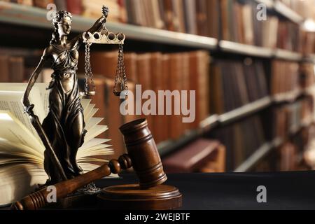 Gesetz. Statue von Lady Justice, Hammer und offenes Buch auf schwarzem Tisch drinnen, Platz für Text Stockfoto