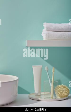 Innenraum eines modernen Badezimmers mit Zahnbürsten in Glasbecher, Kopfhaut-Massagebürste, Handtuch und Hautpflegeprodukt auf blauem Hintergrund. Kunststoffrohr unLabe Stockfoto