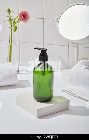 Eine grüne Flasche ohne Etikett auf dem quadratischen Podium, Modell-Körperpflegeprodukt mit Pumpdüse auf weißem Tisch im Badezimmer. Weiße Handtücher, Blumenbasis und mir Stockfoto