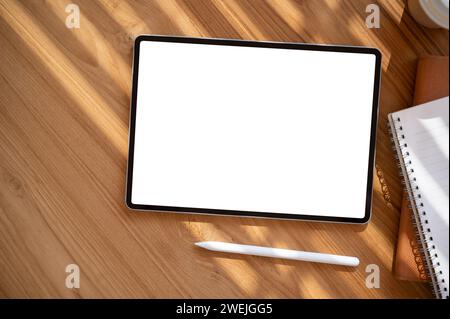 Draufsicht eines digitalen Tablet-Mockups mit weißem Bildschirm auf einem Holztisch mit einem Tablet-Stift und Schreibwaren. Arbeitsbereich, Schreibtisch Stockfoto