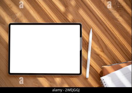 Draufsicht eines digitalen Tablet-Mockups mit weißem Bildschirm auf einem Holztisch mit einem Tablet-Stift und Schreibwaren. Arbeitsbereich, Schreibtisch Stockfoto