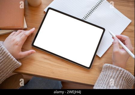 Draufsicht einer Frau, die ein digitales Tablet an ihrem Schreibtisch verwendet. Ein digitales Tablet mit weißem Bildschirm auf einem Holzschreibtisch. Menschen- und Technologiekonzepte Stockfoto