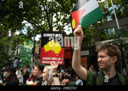 26. Januar 2024, Melbourne, Australien. Ein Demonstrant hält Schilder, eines mit der Flagge der Aborigines kombiniert mit der palästinensischen Flagge und das andere mit der Aufschrift „Always Was, Always will Be Aboriginal Land“, während sie sich gegen den Australia Day oder Invasion Day mit einer Menschenmenge von etwa 30.000 anderen versammeln. Quelle: Jay Kogler/Alamy Live News Stockfoto