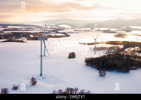 Panoramablick auf Windturbinen, die bei Sonnenuntergang im Winterfeld stehen. Erzeugung von sauberem Strom. Stockfoto