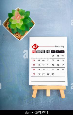 2024. Februar Kalenderseite und Pflanztopf auf blauem hölzernem Hintergrund. Stockfoto