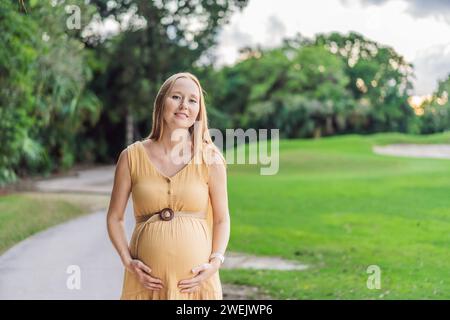 Ruhige Szene, in der eine schwangere Frau friedliche Momente im Park genießt, die Ruhe der Natur genießt und während ihrer Schwangerschaft Trost findet Stockfoto