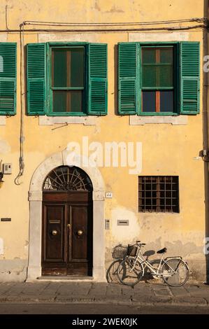 Fahrrad vor der Gebäudefassade mit gelben Wänden und grünen Fensterläden, Pisa, Toskana, Italien Stockfoto