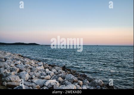 Eine Person, die während des Sonnenuntergangs an der felsigen Küste spaziert Stockfoto