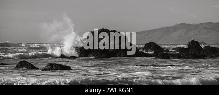 Ein schwarz-weißer Schuss Wasser, das auf Felsen im Ozean spritzt. Stockfoto