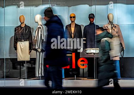Eine Gruppe von Einzelpersonen, die an einem Geschäft vorbeischlendern, das mit einer fesselnden Schaufensterpuppe geschmückt ist. Stockfoto