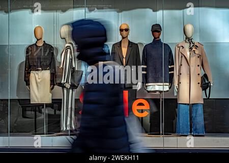 Eine Gruppe von Einzelpersonen, die an einem Geschäft vorbeischlendern, das mit einer fesselnden Schaufensterpuppe geschmückt ist. Stockfoto