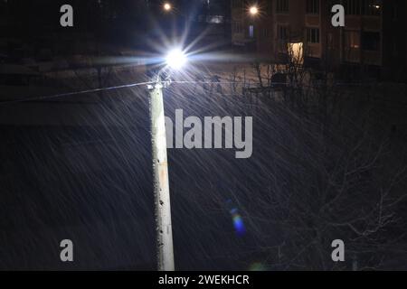 Im Licht einer Straßenlaterne ist fallender Schnee sichtbar, der vom Wind angetrieben wird. Stockfoto
