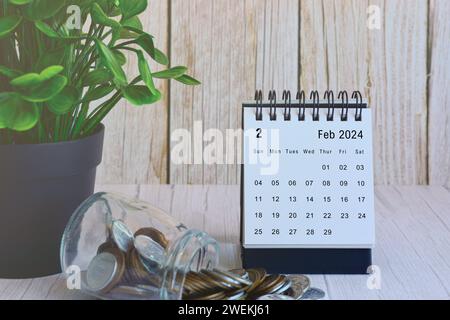 Schreibtischkalender Februar 2024 mit Münzstapel und Topfpflanze auf Holztisch. Terminkonzept für Unternehmen und Finanzen. Stockfoto