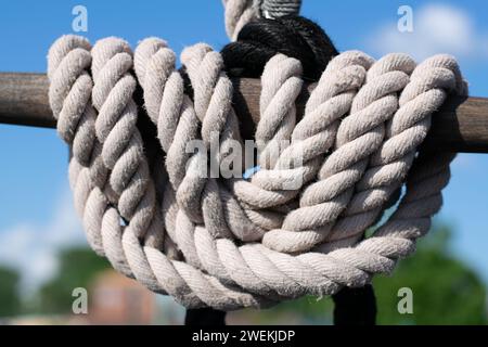 Ein dickes, weißes Seil ist fachmännisch um einen festen Anlegepfosten gewickelt und bildet einen Kontrast zum leuchtend blauen Himmel eines ruhigen Tages. Stockfoto