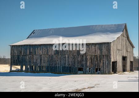 Die veraltete Struktur einer großen Holzscheune wird durch das helle, klare Sonnenlicht, das vom umliegenden Schnee reflektiert wird, verstärkt. Stockfoto