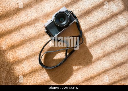 Retro-Kamera auf Plüschkarot mit Sonnenstrahlen durch Fensterjalousien. Hintergrund Stockfoto
