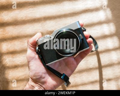 Eine Kamera im Retro-Stil in der Hand eines Mannes vor dem Hintergrund eines Plüschkarions in den Sonnenstrahlen durch die Jalousien. Hintergrund Stockfoto
